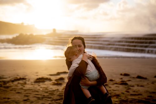 Free A mother embraces her child during sunset on a sandy beach, conveying warmth and love. Stock Photo