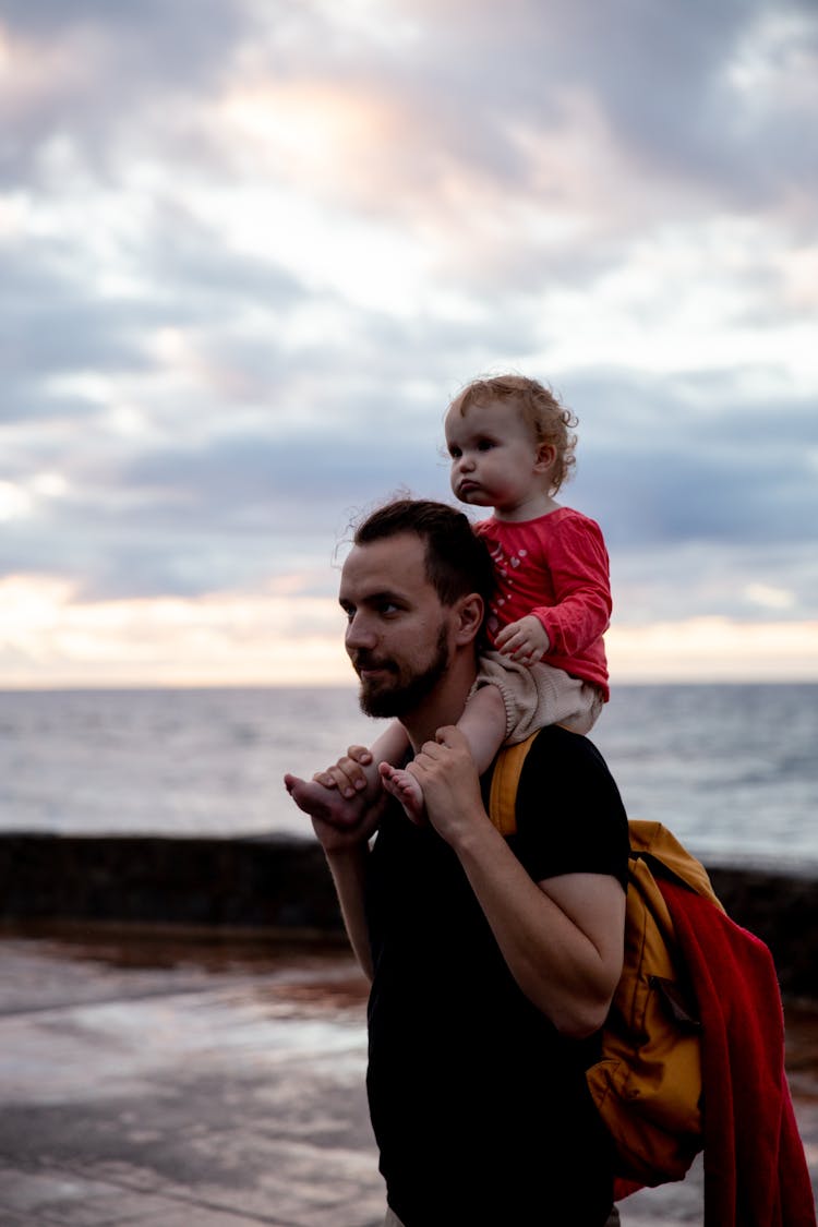 Man In Black Shirt Carrying Little Girl On His Shoulder