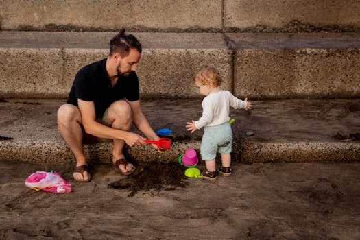 A father and toddler enjoying a bonding moment playing with beach toys on a sandy shore.