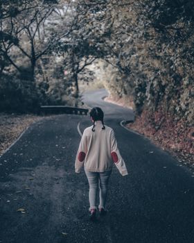 一位孤独的女人走在蜿蜒的森林道路上，四周满是秋叶