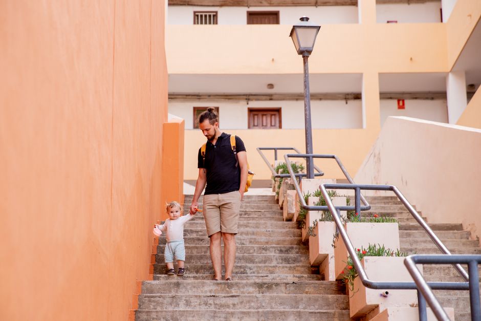 Un papá toma de la mano a su niño pequeño en escaleras comunitarias al aire libre durante el día.