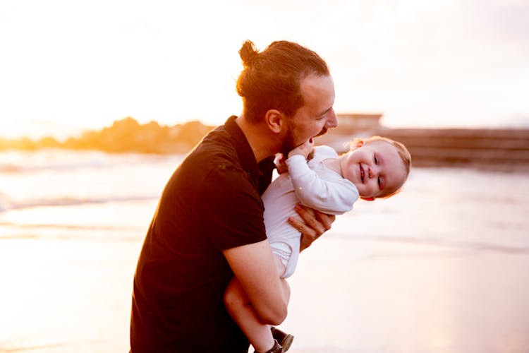 Man In Black T-shirt Carrying Baby In White Onesie 