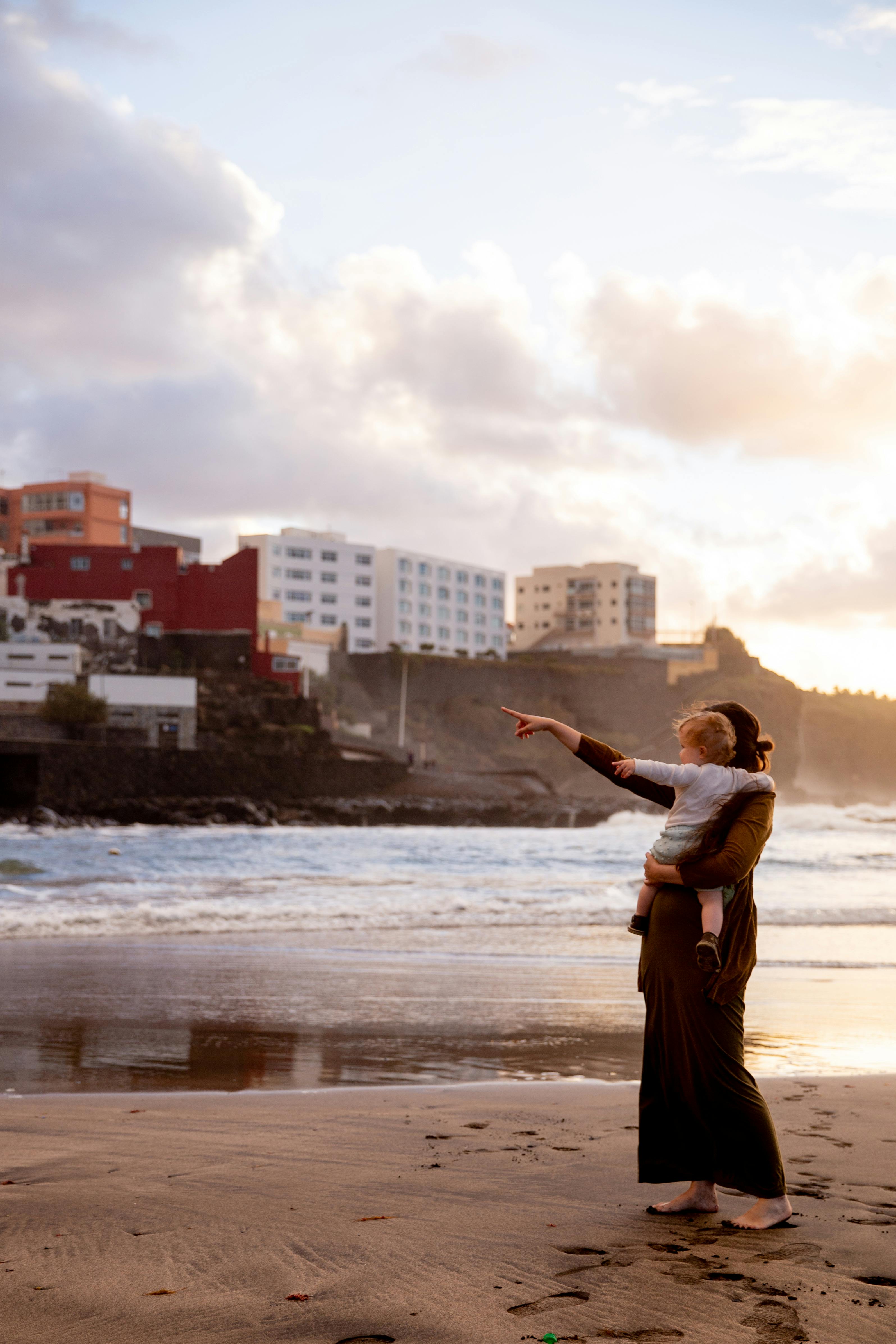 woman in brown dress standing on seashore carrying her baby