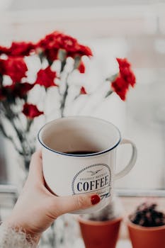 手拿一个带有文字的咖啡杯，背景是红花