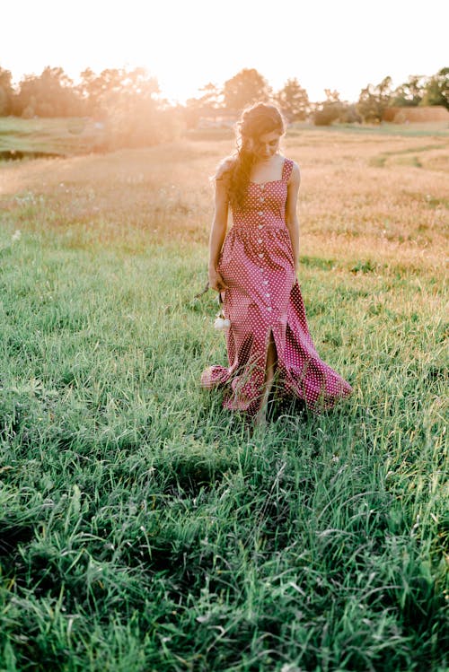 Woman in Polka Dot Dress Walking on Green Grass Field