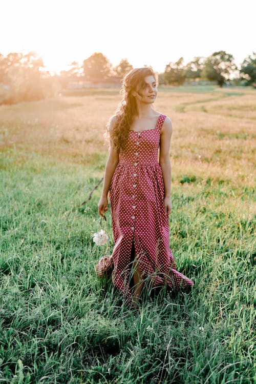 緑の芝生のフィールドに立っている赤と白の水玉模様のドレスの女性
