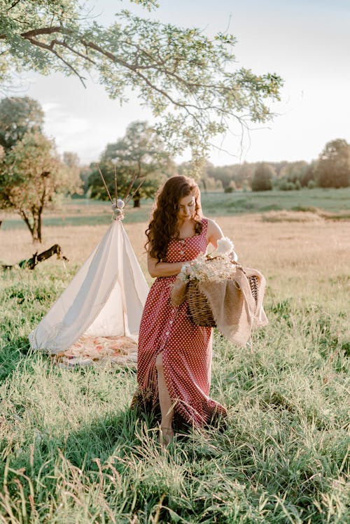 Woman in Red and White Dress Holding White Bouquet on Green Grass Field