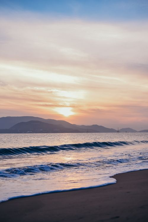 Free Peaceful sunset view with waves crashing on the shore and mountains in the background. Stock Photo