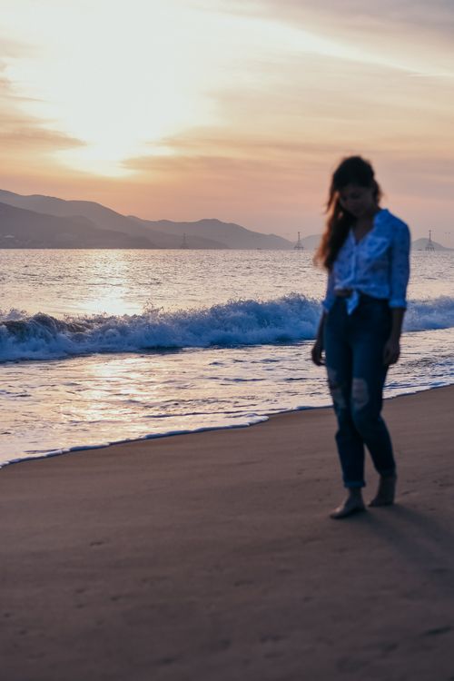 Free A serene silhouette of a woman walking along the beach during a stunning sunset, with waves gently crashing. Stock Photo