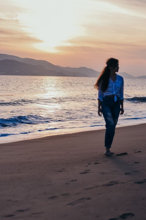 Free A woman strolls along a beach at sunset, enjoying the tranquil ocean scenery. Stock Photo