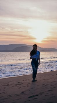 Silhouette of a woman walking along the beach during a serene sunset.