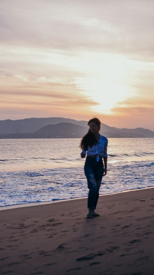 Free Silhouette of a woman walking along the beach during a serene sunset. Stock Photo