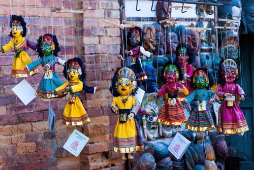 Free A vibrant display of traditional Rajasthani puppets hanging against a rustic brick wall. Stock Photo