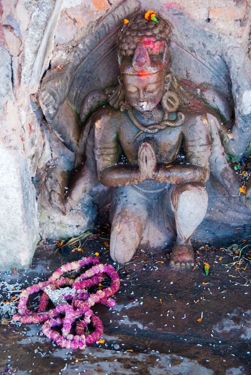 Free A serene stone statue in a meditative pose, adorned with vibrant flower garlands in a historic setting. Stock Photo