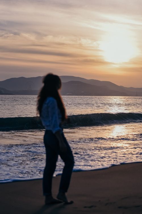 Free Silhouette of a woman walking along the beach during a stunning sunset. Stock Photo