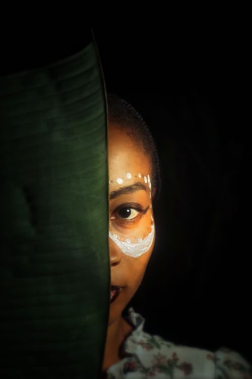 Free Artistic portrait featuring tribal face paint with a large leaf creating a dramatic effect against a dark background. Stock Photo