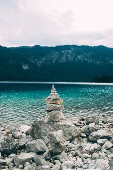 Peaceful lake view with stacked stones against mountain backdrop, ideal for nature themes.