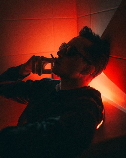 Free Portrait of a man in moody, red lighting, smoking a cigarette indoors. Stock Photo