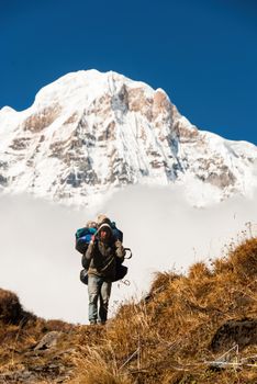 A determined hiker climbs a trail with Annapurna Mountain looming majestically in the background.