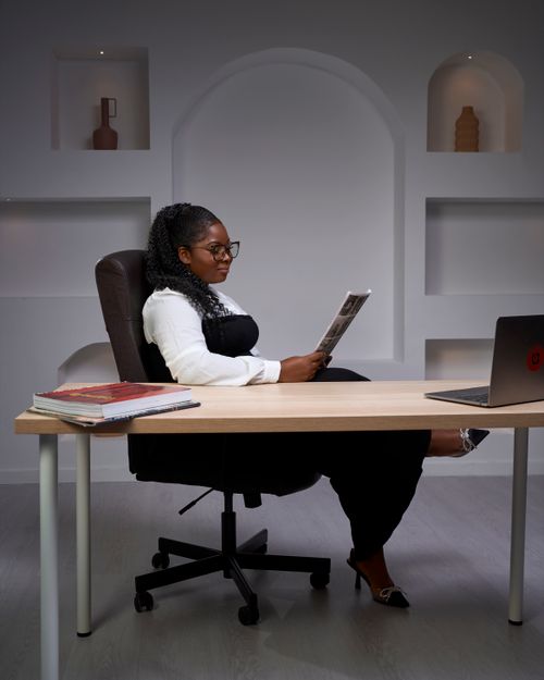 Free Woman sitting at a desk in a modern office setting, reading a newspaper. Stock Photo