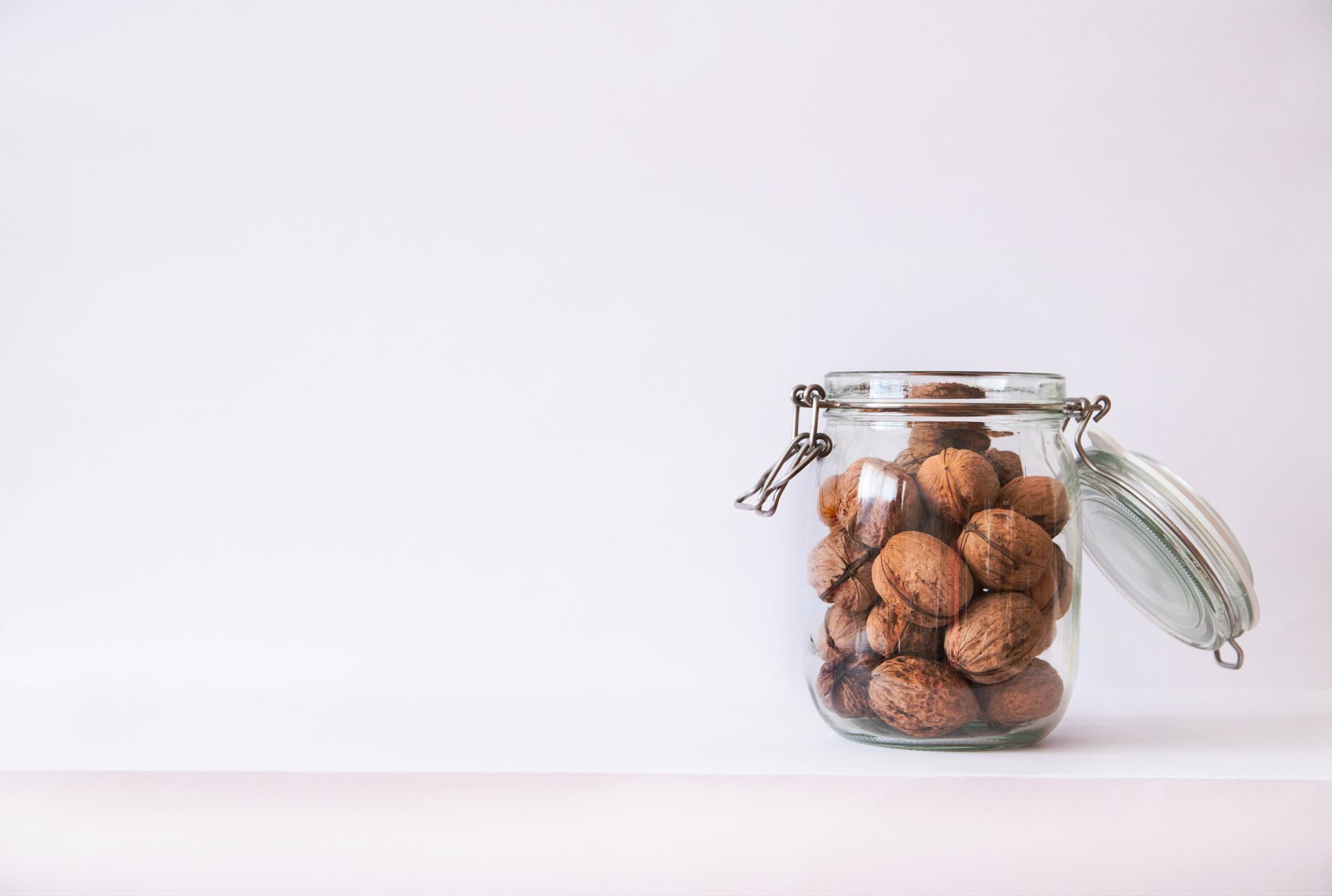 Glass jar filled with walnuts against a white background. Simple and minimalistic still life setup.