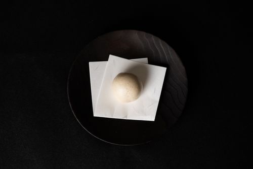 Free A minimalist photo of a single Japanese mochi placed on a black plate against a dark background. Stock Photo