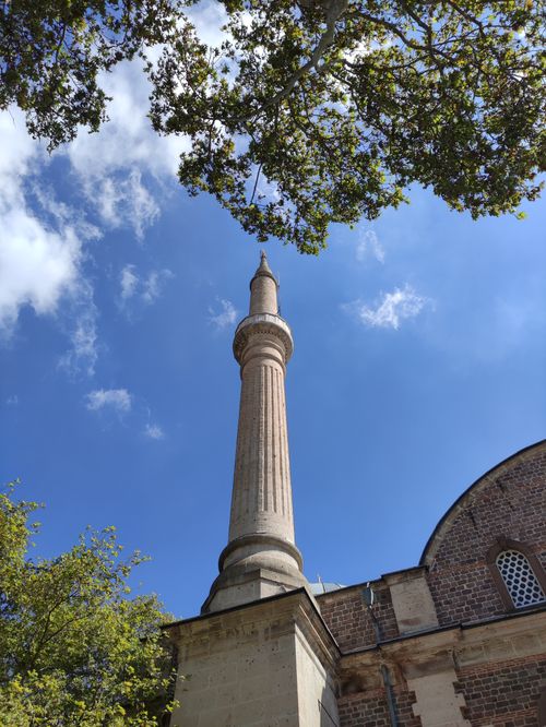 Free Upward view of a historic mosque minaret with a vibrant blue sky and trees framing the structure. Stock Photo