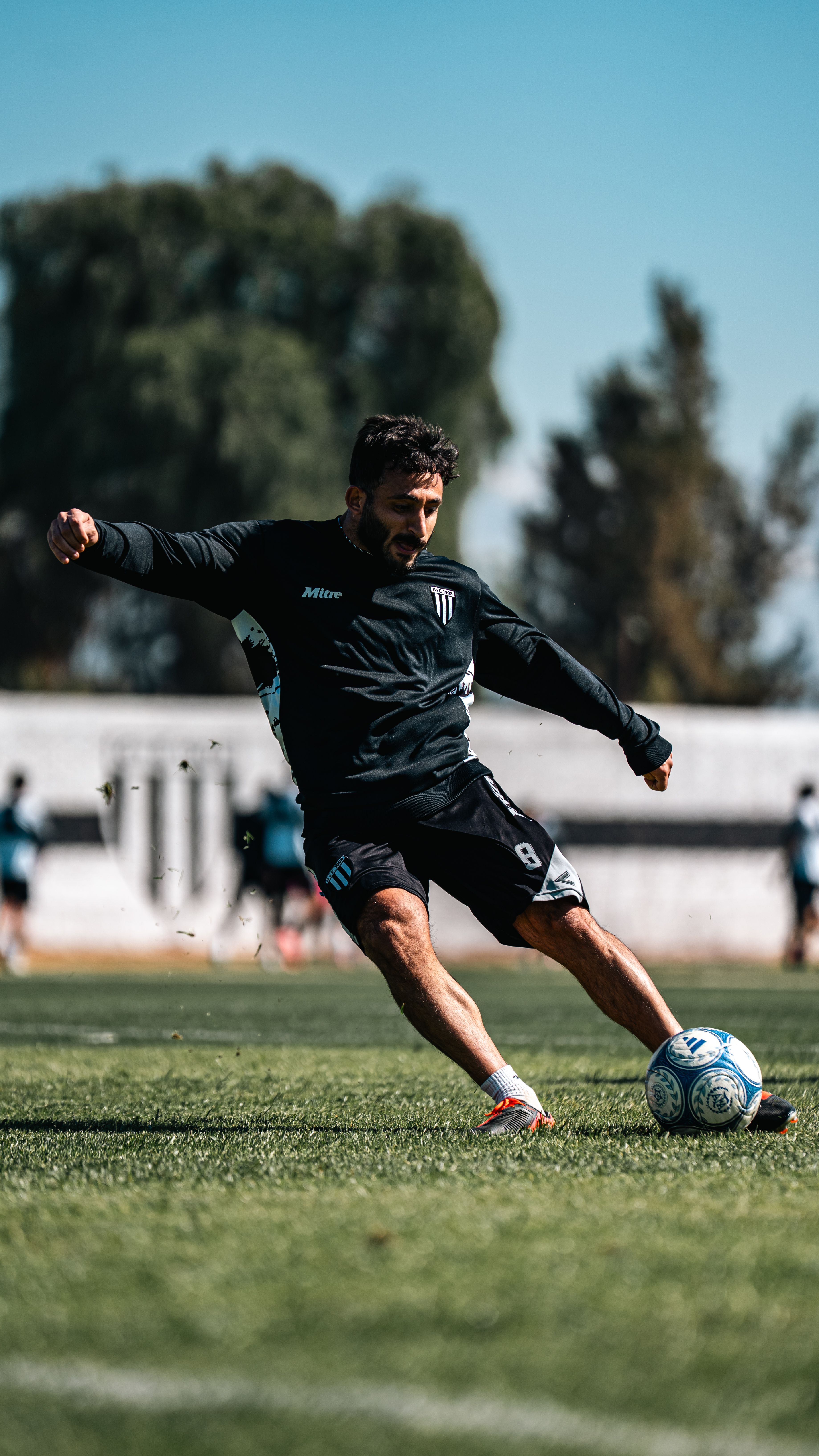 Energetic football player in motion capturing an intense kick during training on a sunny day.