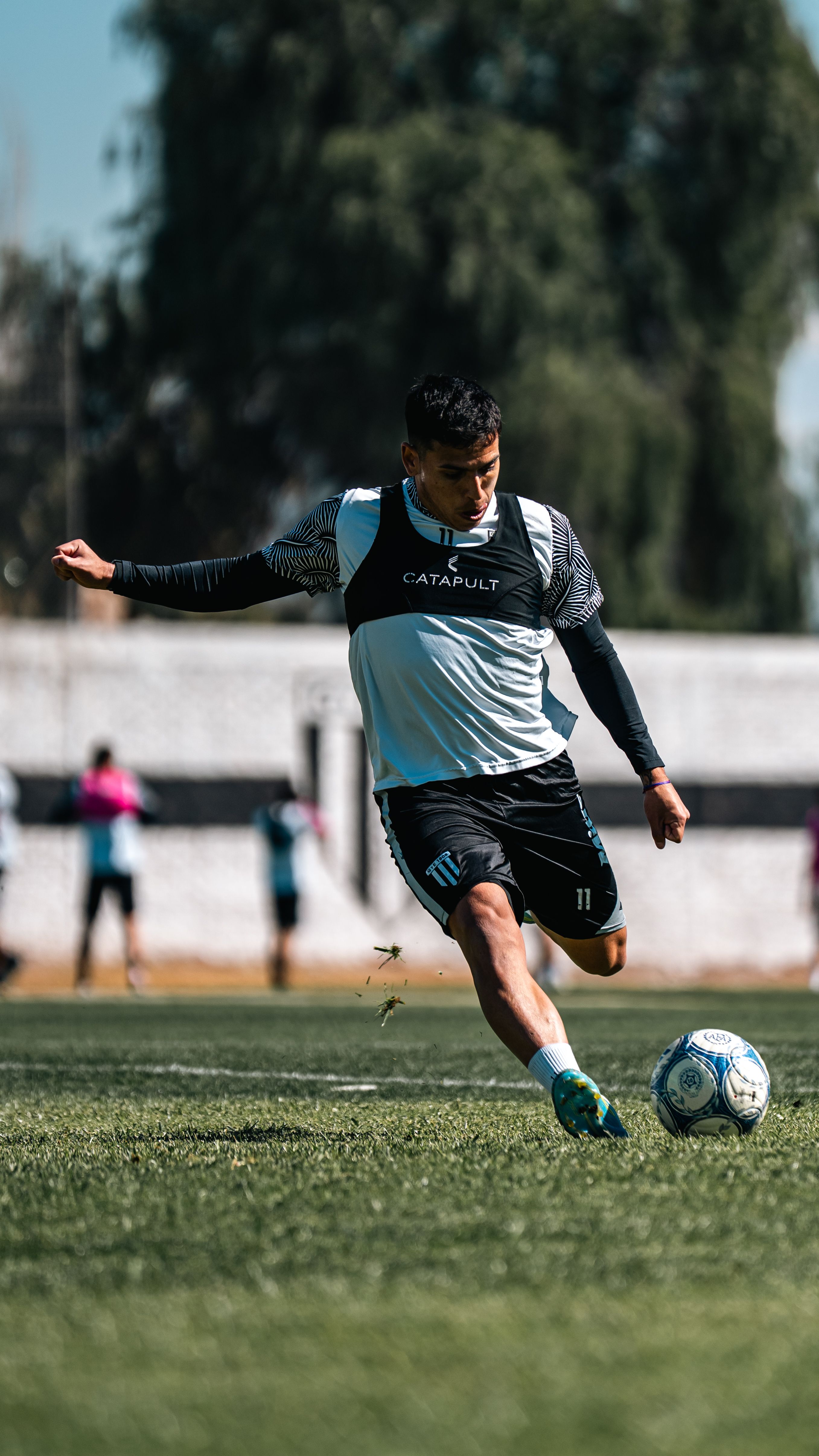 Dynamic image of a soccer player kicking the ball during a daytime match on a grassy field.