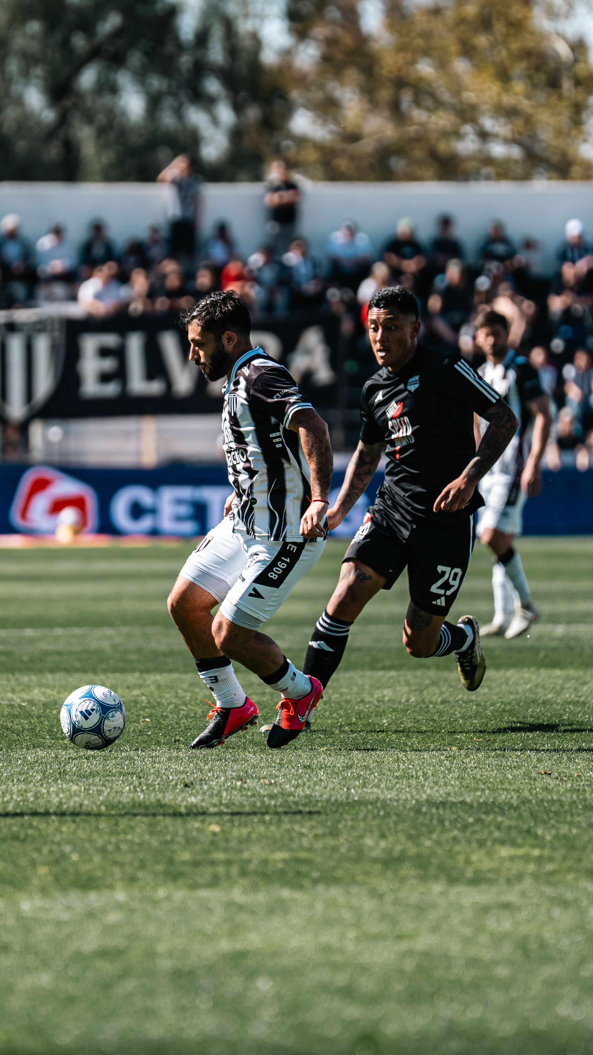 Two soccer players in action during a competitive match on a sunny day.