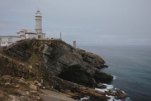 Free Lighthouse perched on rugged cliffs in Santander, Spain, with the sea as a backdrop. Stock Photo