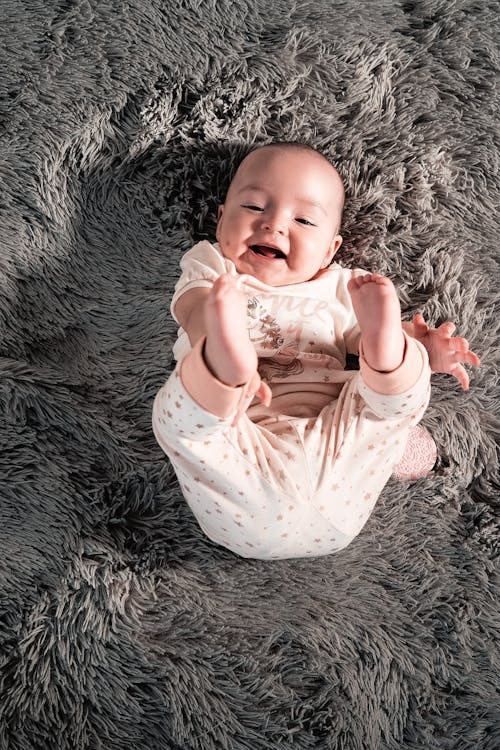 A baby smiling and laying on a fur carpet.