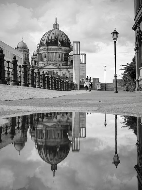 Free Black and white photo of Berlin Cathedral reflecting in a puddle with a bridge path and overcast sky. Stock Photo