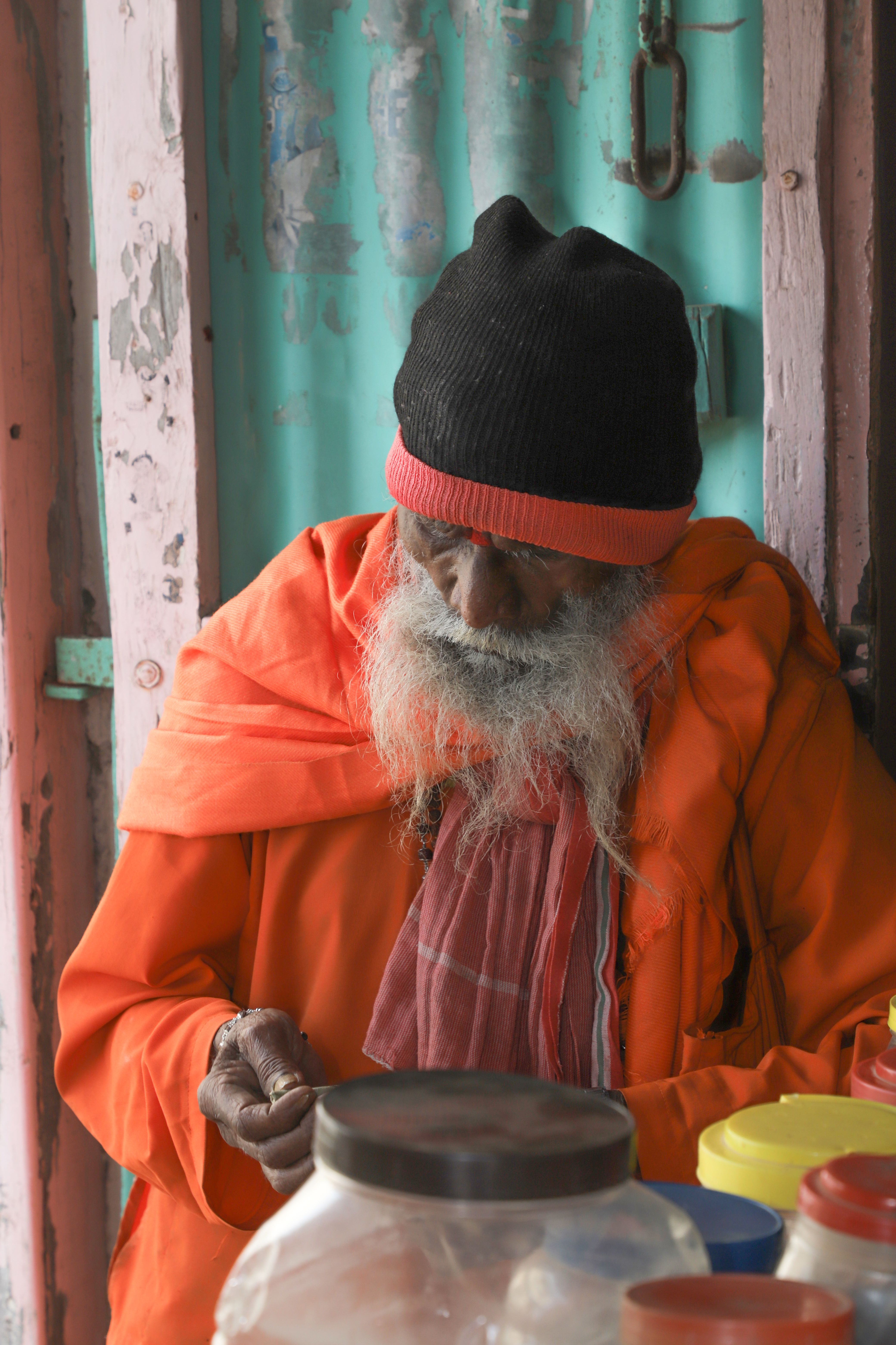An elderly man in traditional orange attire with white hair and beard sitting pensively in Gujarat.