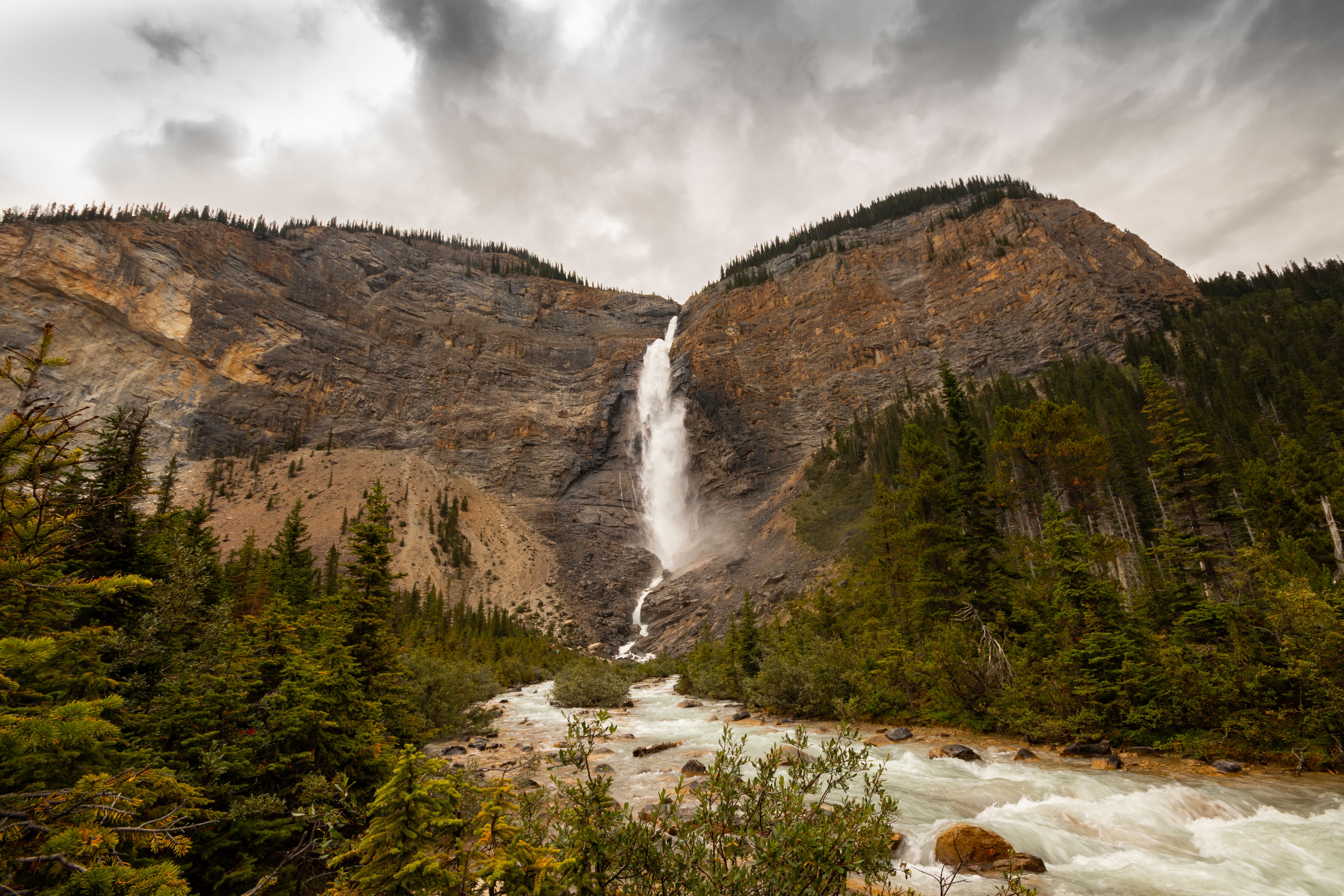 A scenic view of a waterfall cascading down rocky mountains surrounded by lush forest in Banff National Park.