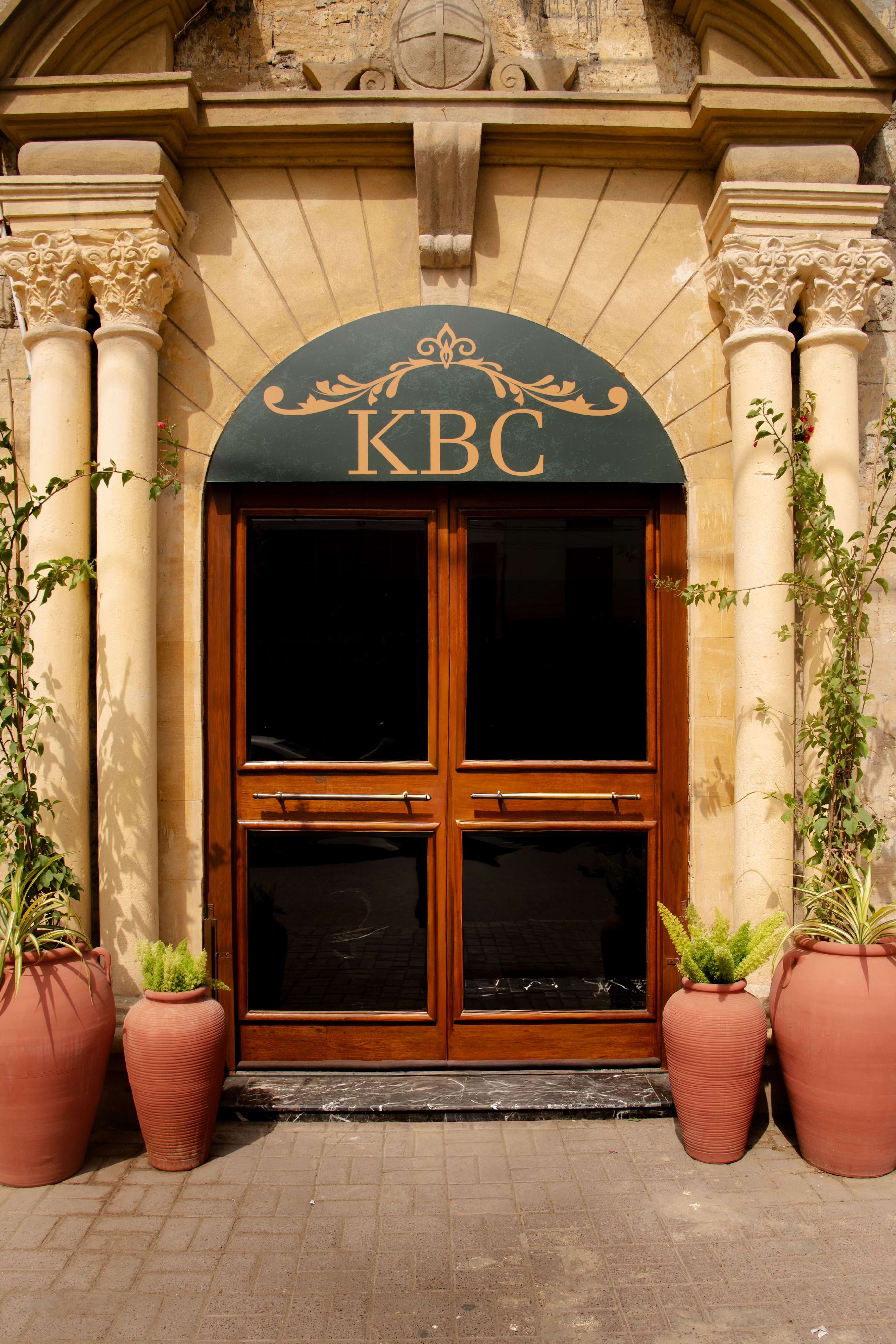Close view of ornate building facade featuring decorative columns and green awning reading 'KBC'.