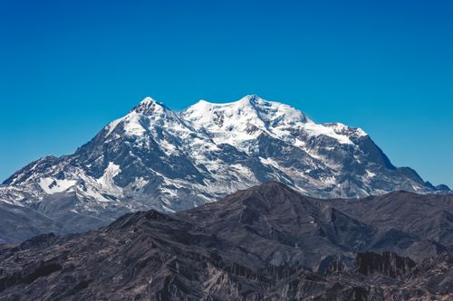Free Snow-capped Mount Illimani stands tall under a clear blue sky in the Bolivian Andes. Stock Photo