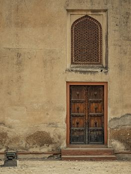 Weathered wooden door and ornate window set in ancient textured wall.