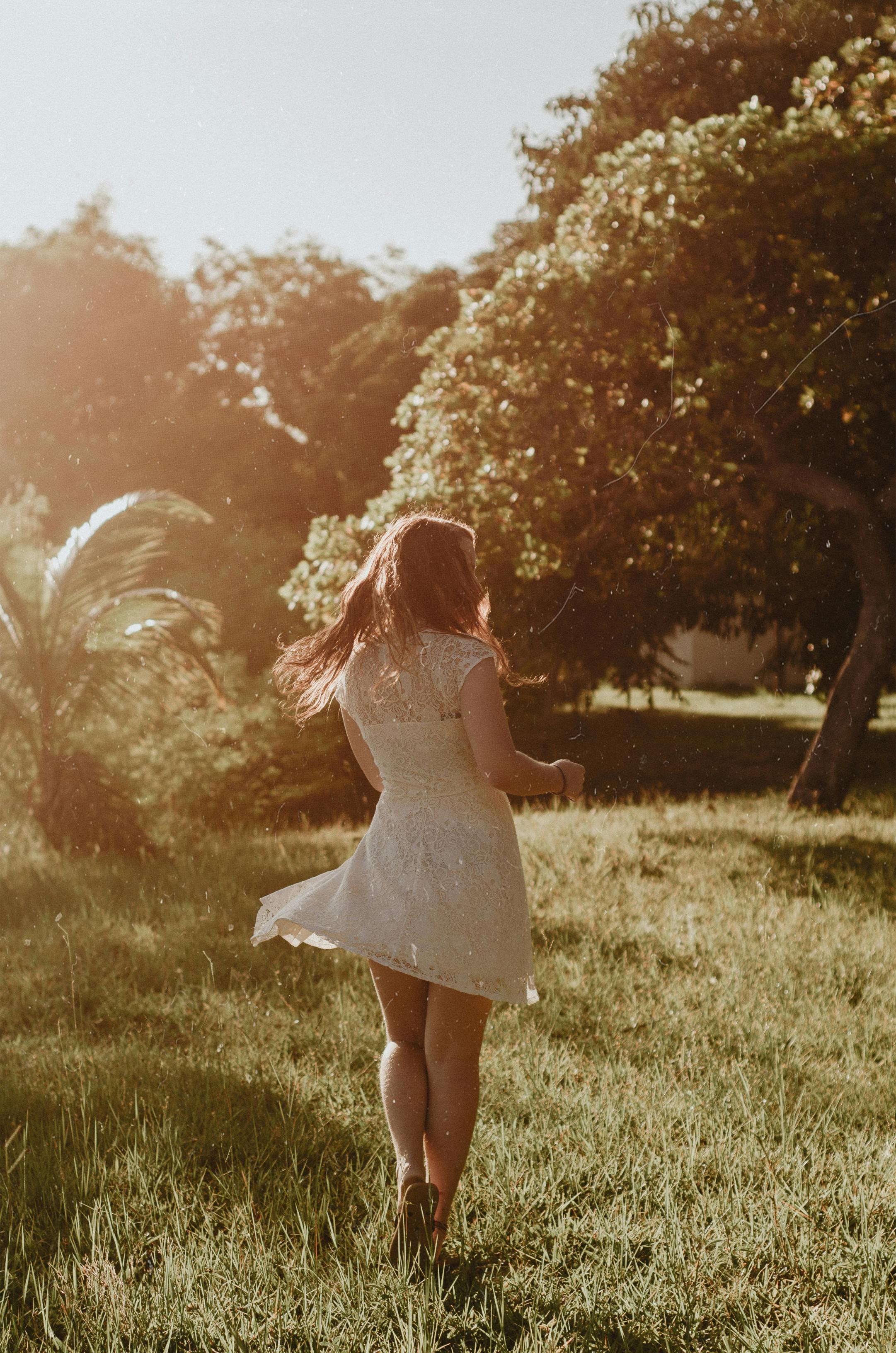 Back view of woman in white dress enjoying a serene field at golden hour.
