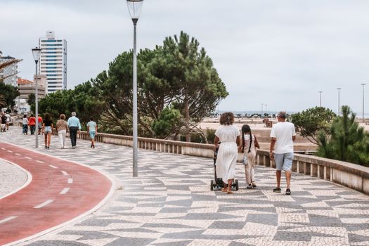 People walking along a beachside promenade with patterned pavement and coastal views.