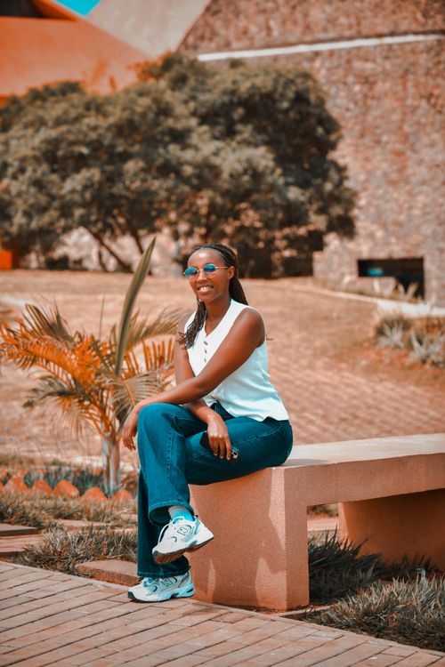 Free A stylish young woman sits on a bench in a serene Rwandan park, enjoying a sunny day. Stock Photo