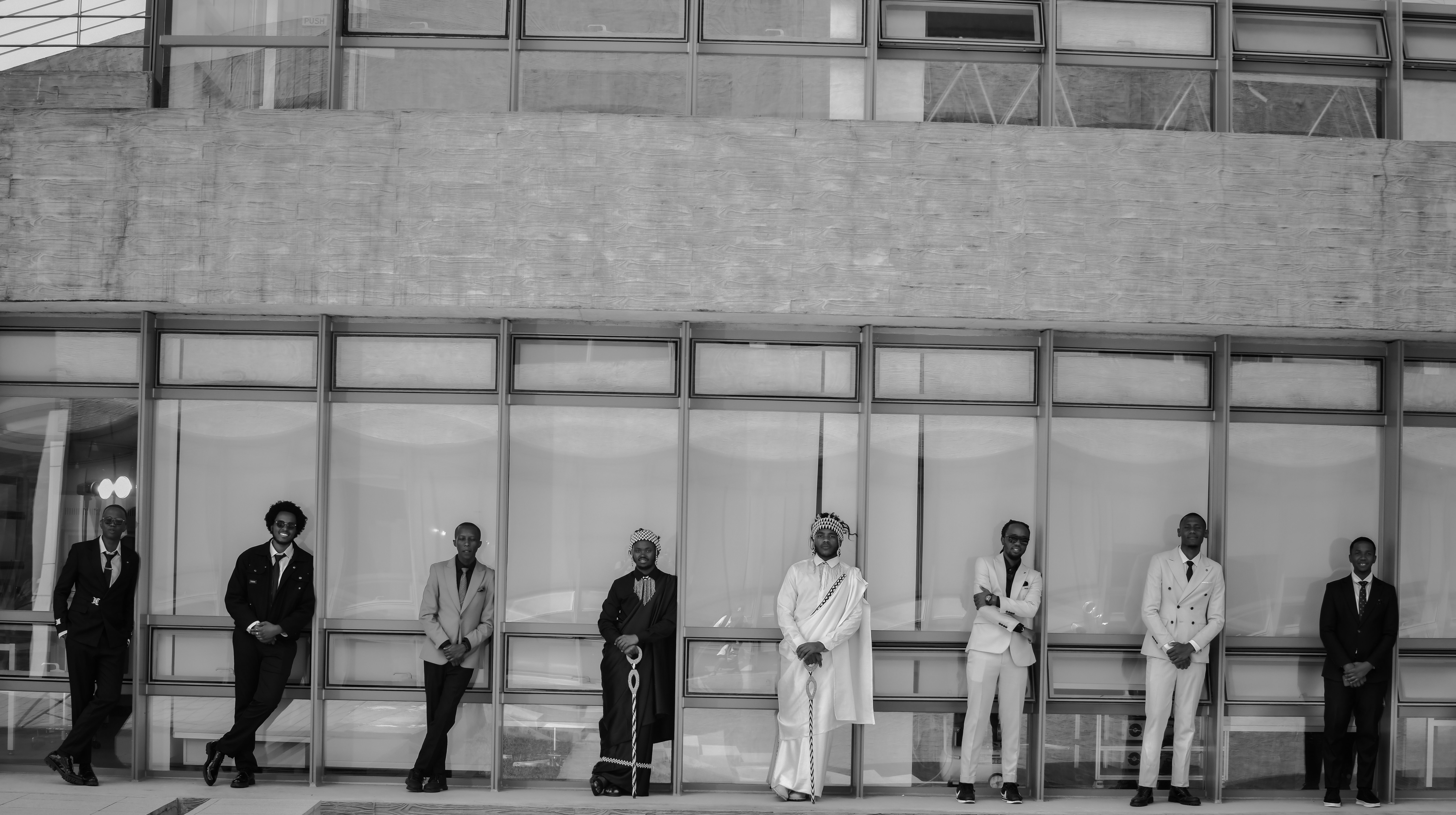 Group of men in various traditional and modern suits posing against a building in Rwanda.