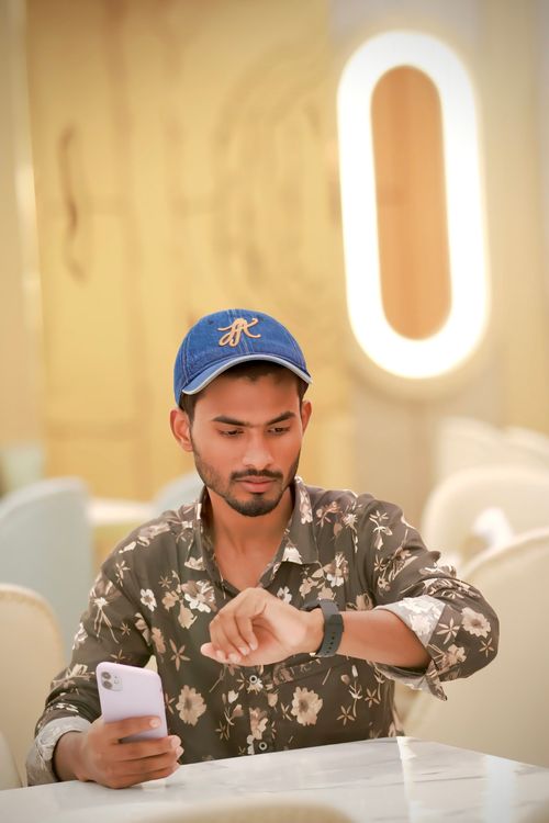 Free A young man with a smartphone checking his smartwatch in a stylish cafe. Stock Photo
