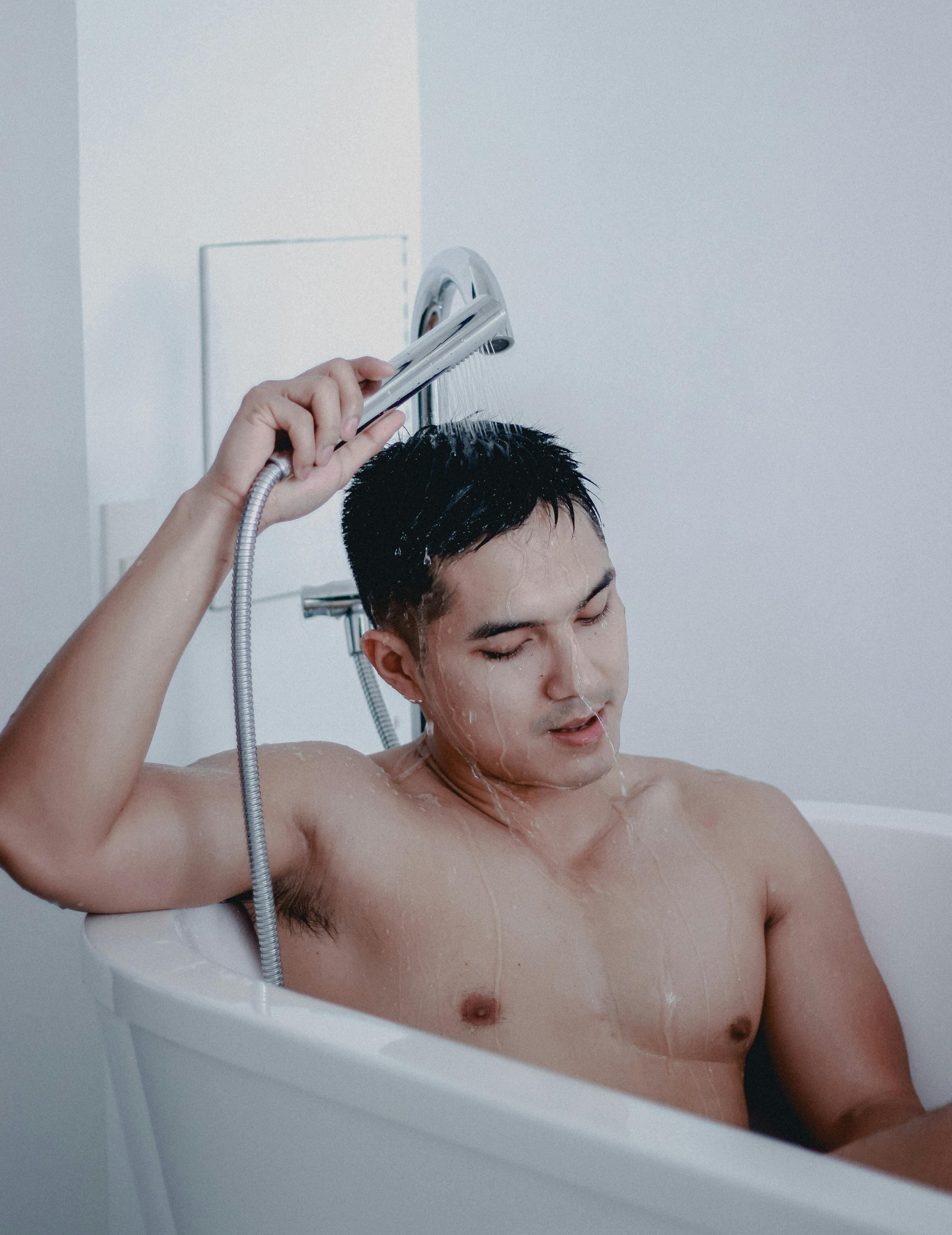 topless man in bathtub holding shower