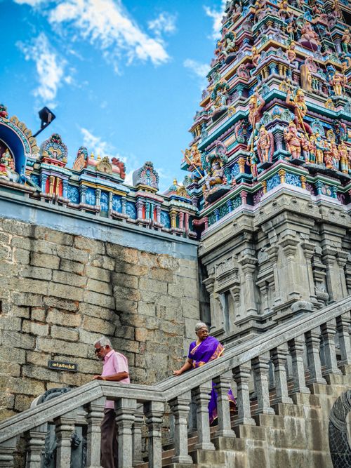 Free Elderly couple ascending stairs at a colorful Hindu temple against a blue sky. Stock Photo