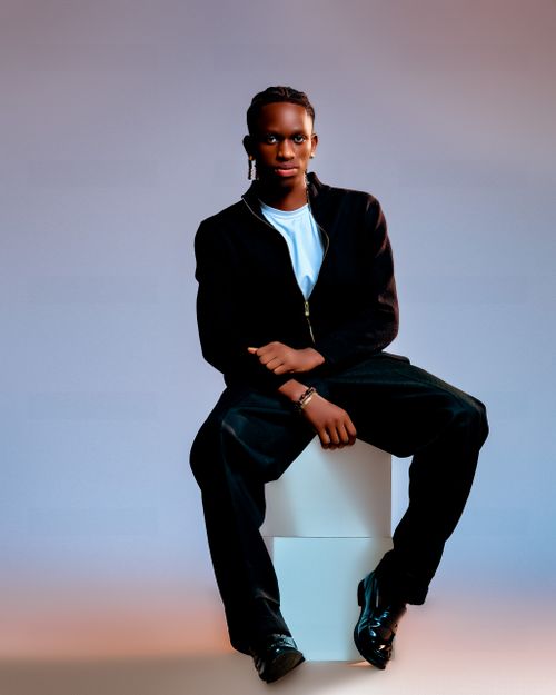 Free Young fashionable man sitting confidently on a white cube against a gradient background. Stock Photo