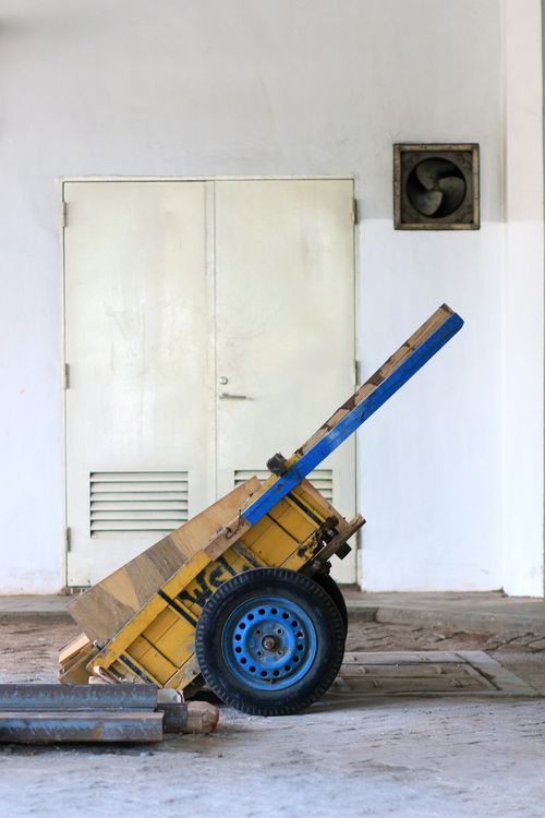 Free An old handcart leaning against an industrial indoor wall with ventilation and door. Stock Photo