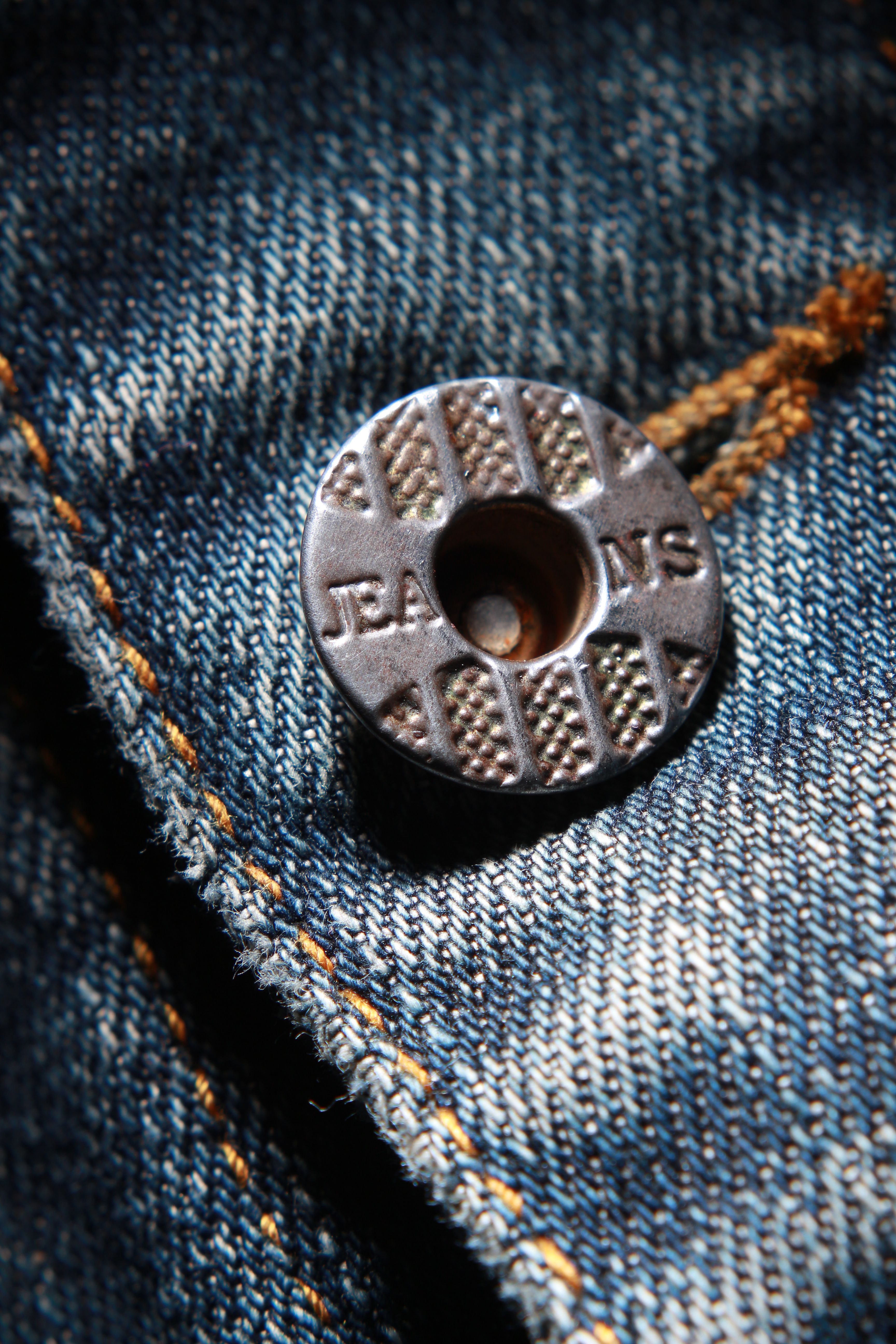 Macro shot of a metal button on blue denim jeans highlighting texture and detail.