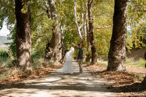 Free A joyful couple dances on a picturesque tree-lined path surrounded by autumn foliage. Stock Photo