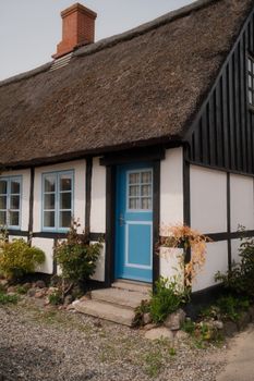 Quaint white and black timber cottage with a thatched roof and blue door, framed by a garden.